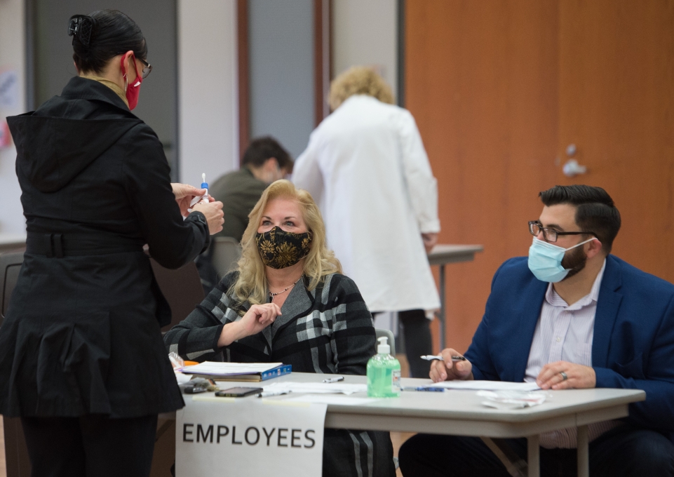 Two employees, seated at table, registering a colleague for screening 